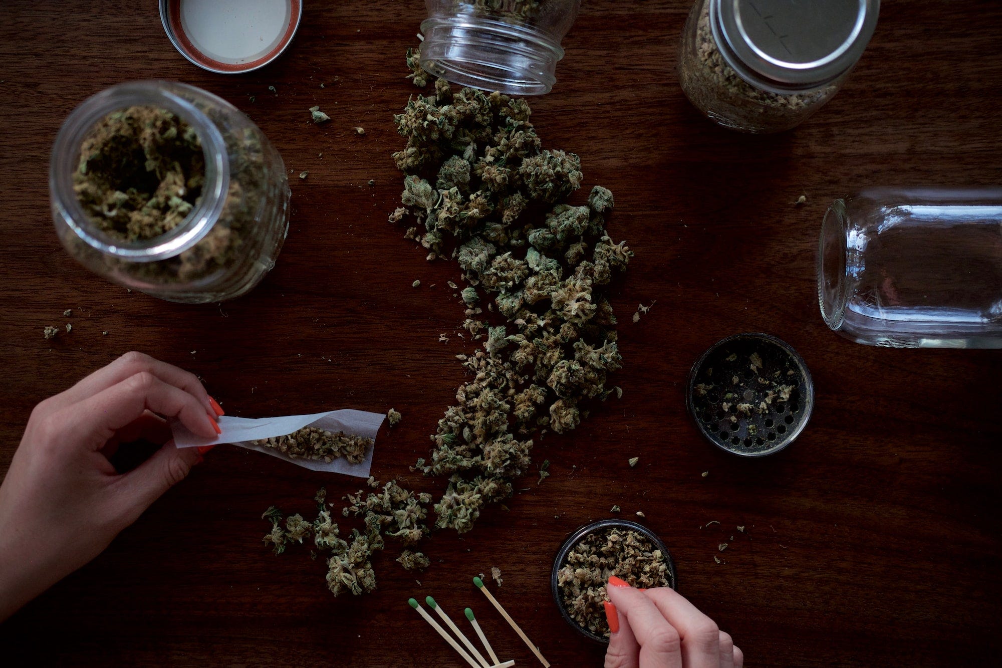 A person rolling cannabis buds into cigarettes with other buds in clear jars