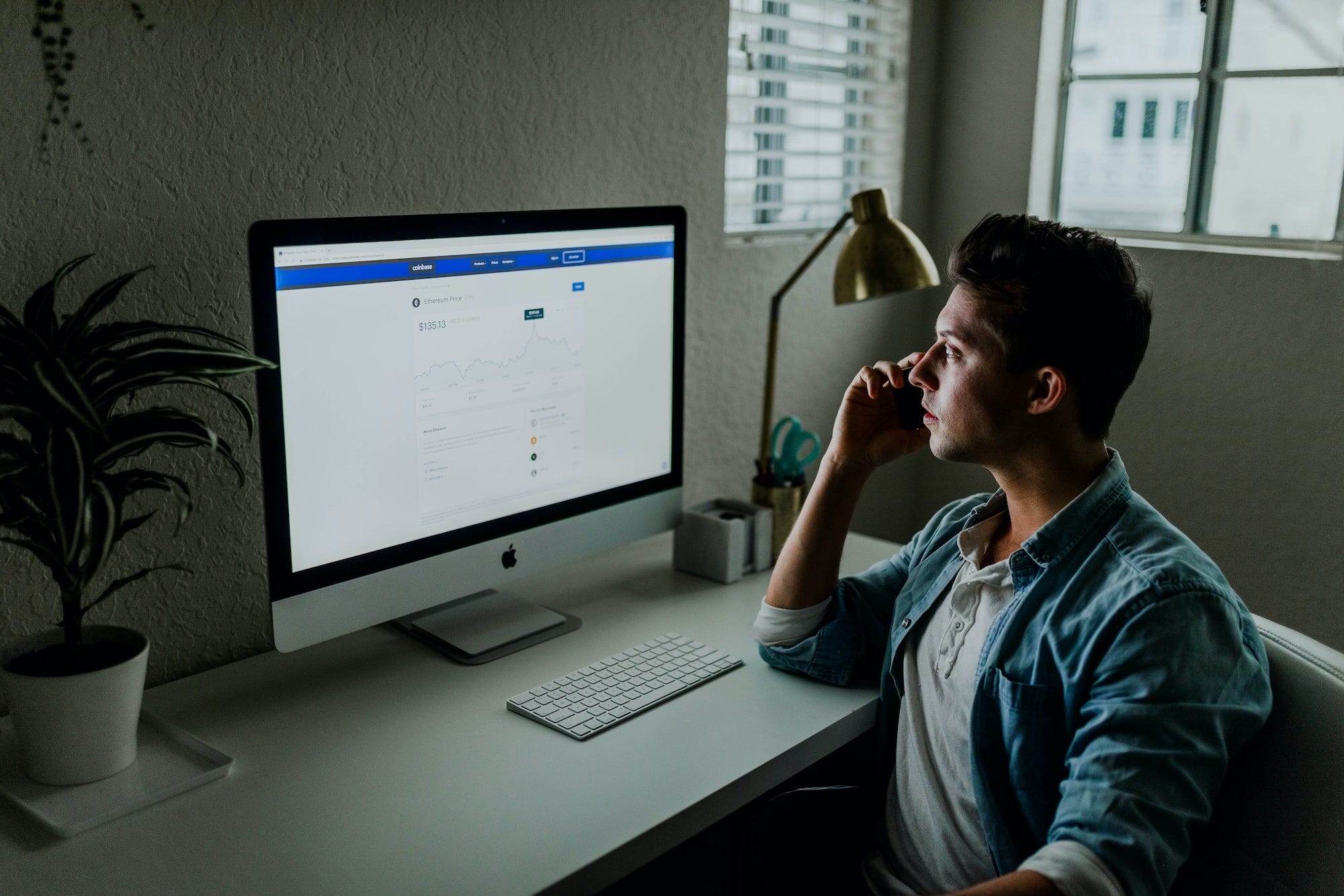 A man speaking on his phone at a desk looking at his computer