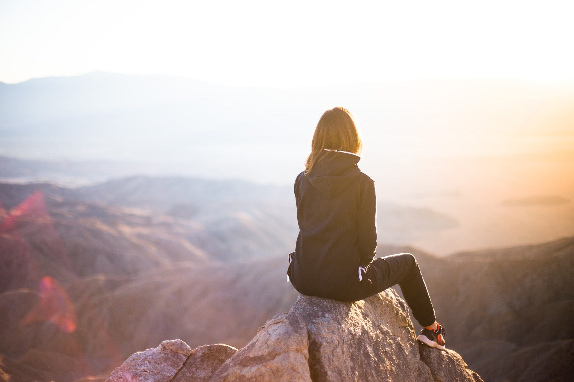 A photo of a woman seating on a rock on top of a mountain range