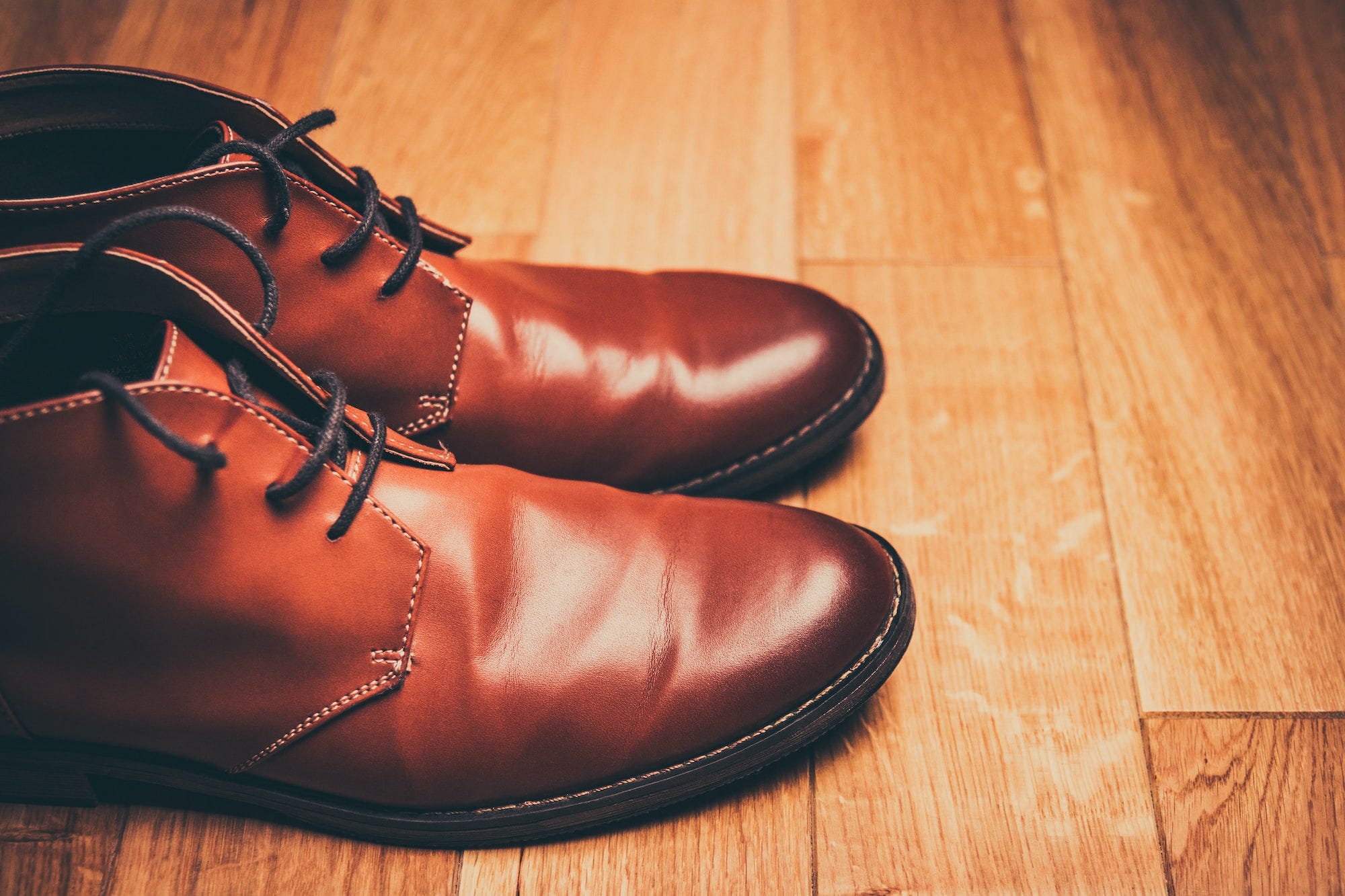 A pair of brown leather boots on a wood floor. Leather shoes should not be washed in a washing machine