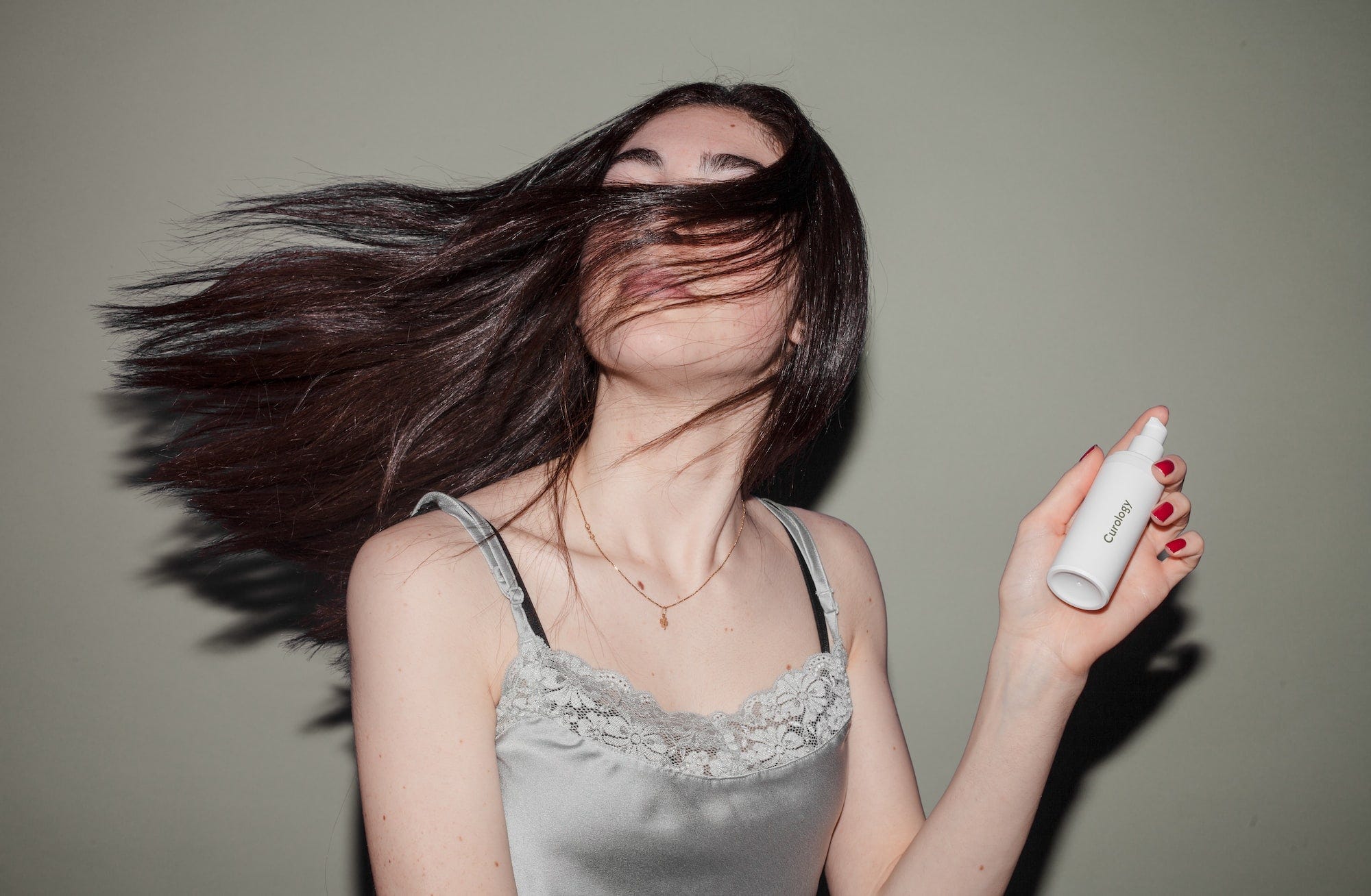 A woman swaying her hair while holding a bottle of hair product