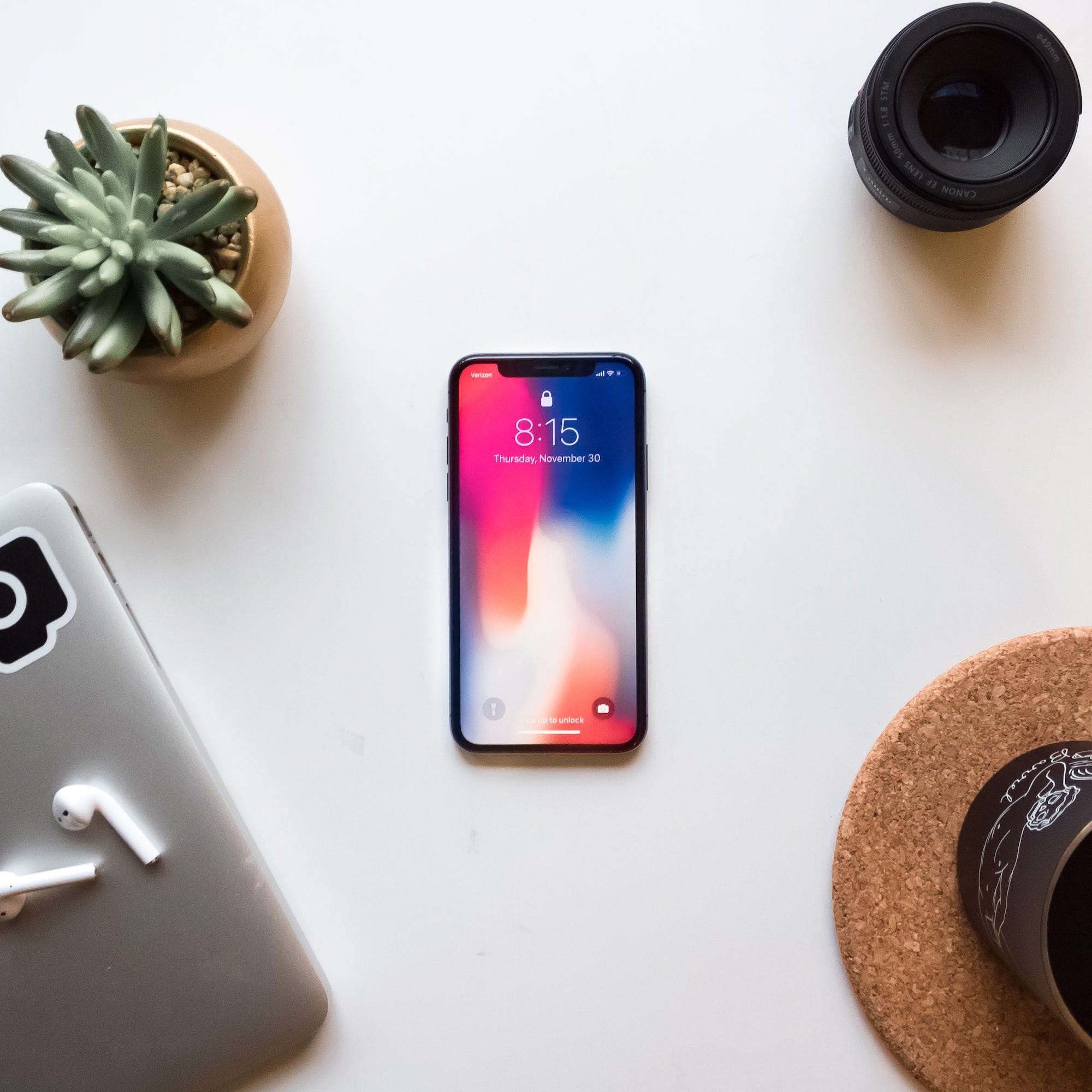 An iPhone on a desk alongside a laptop, a mug, and a plant