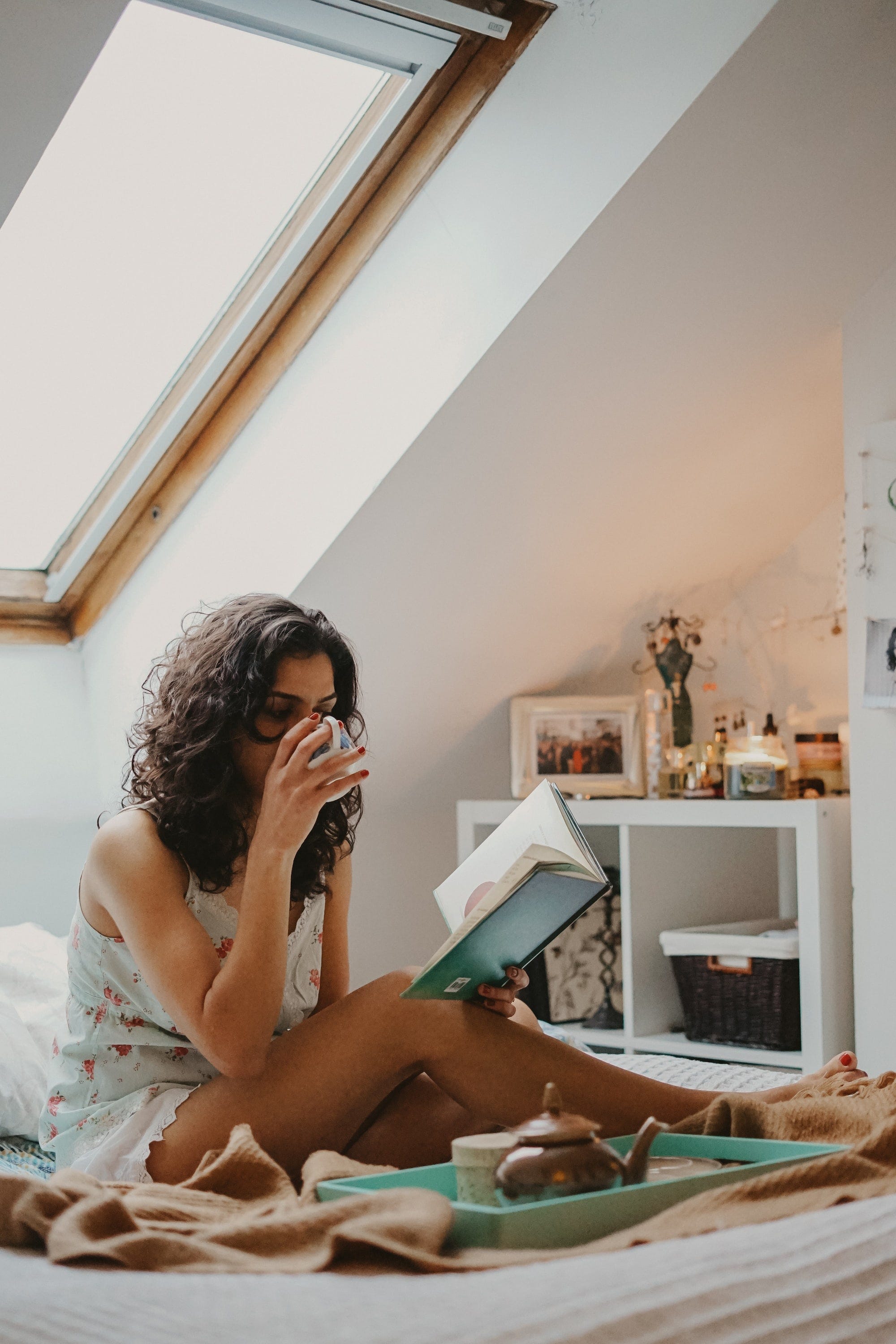 A woman reading a book in bed while drinking Chai