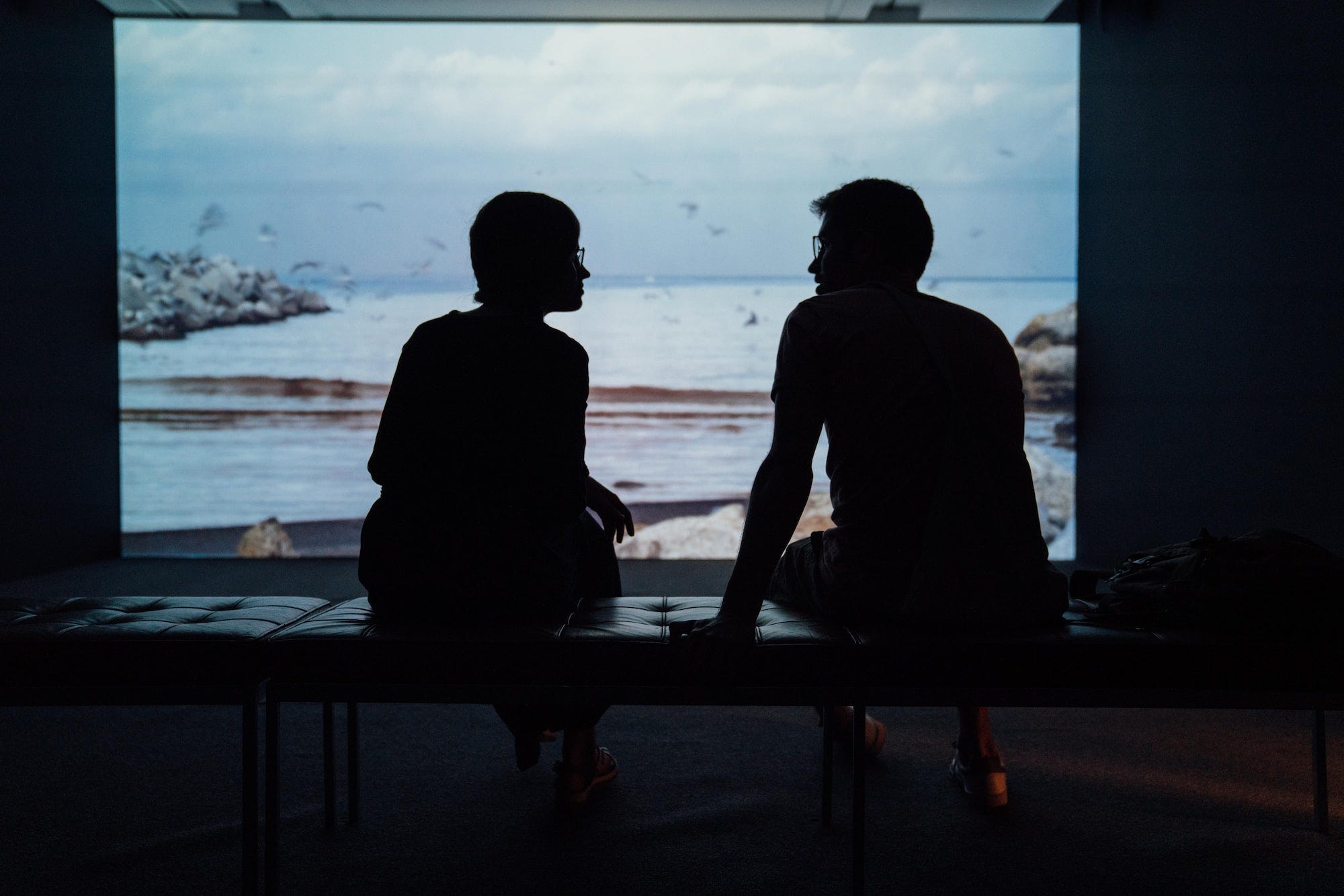 A man and woman sitting on a bench in an art exhibition