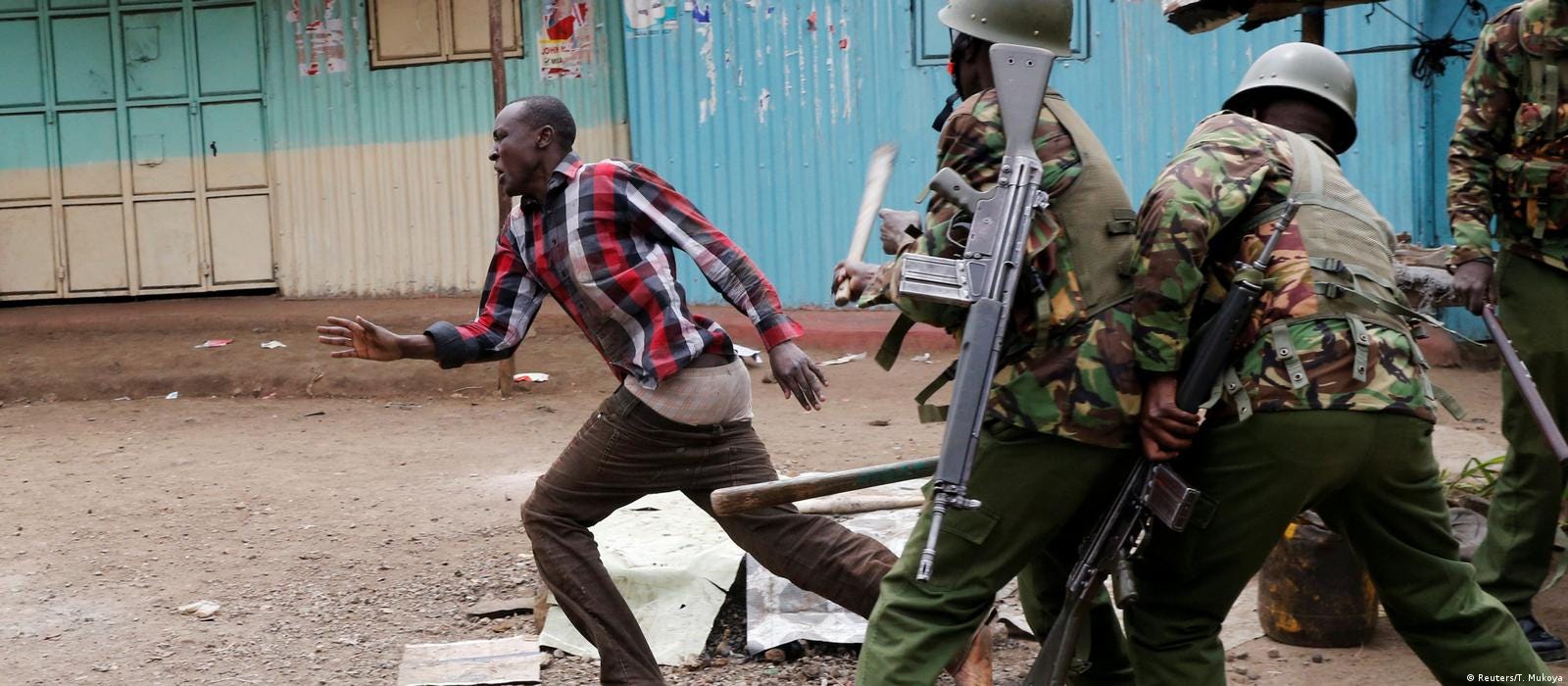 A protestor running from police officers who are clobbering him with batons