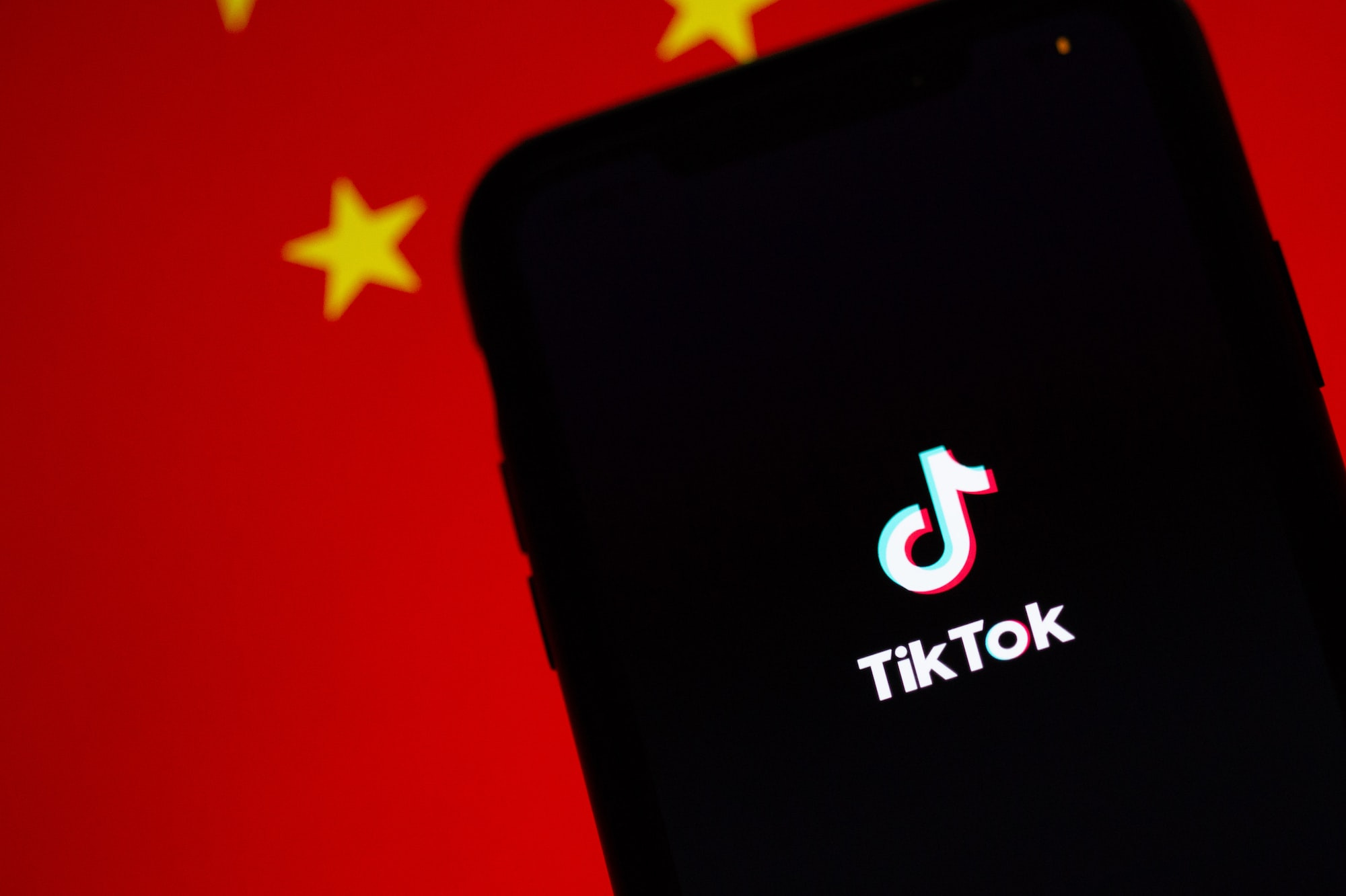 An image of TikTok running on an iPhone with the Chinese flag displayed behind it