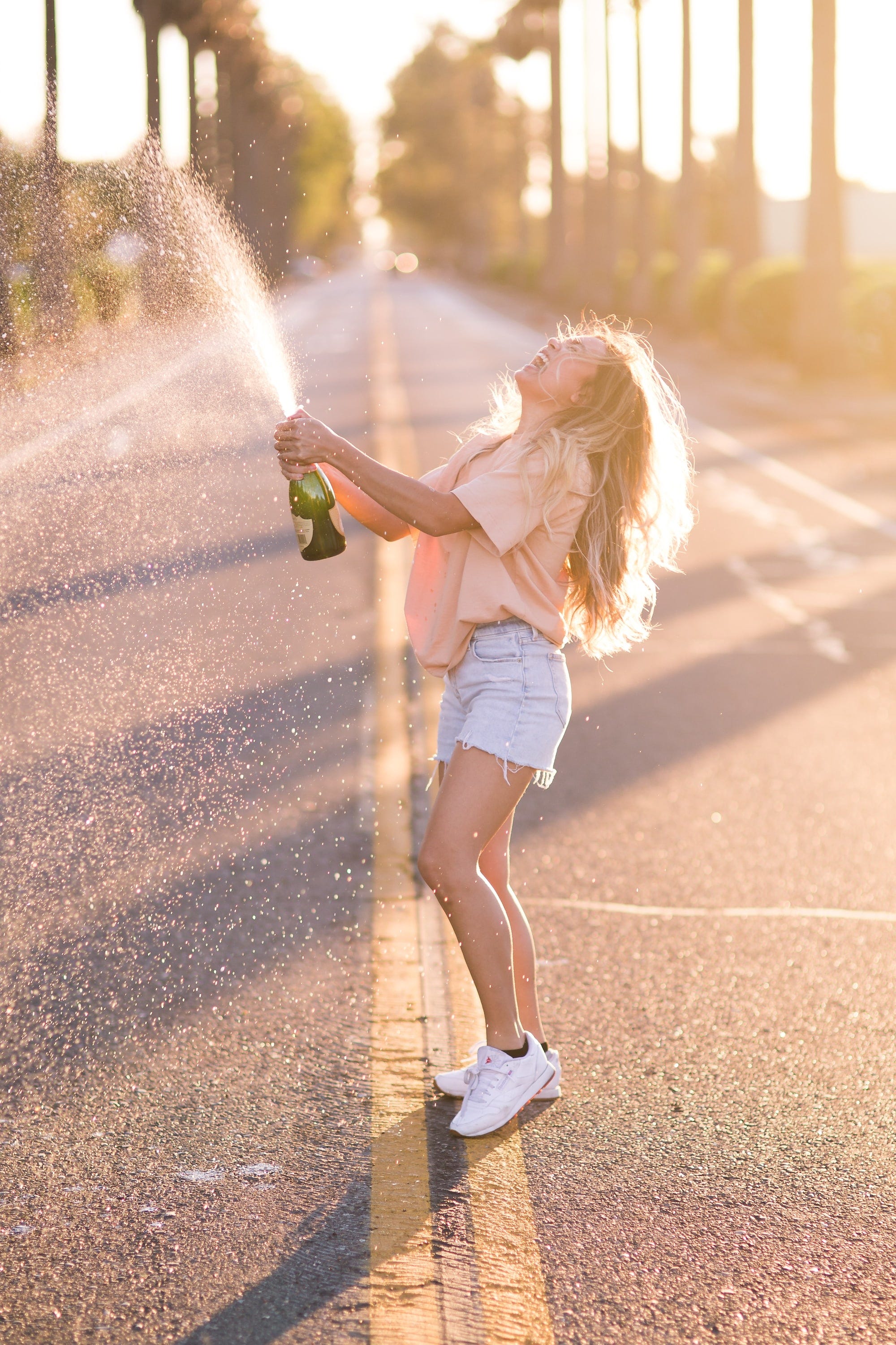 A woman popping a bottle of champagne on the road while happily shouting out