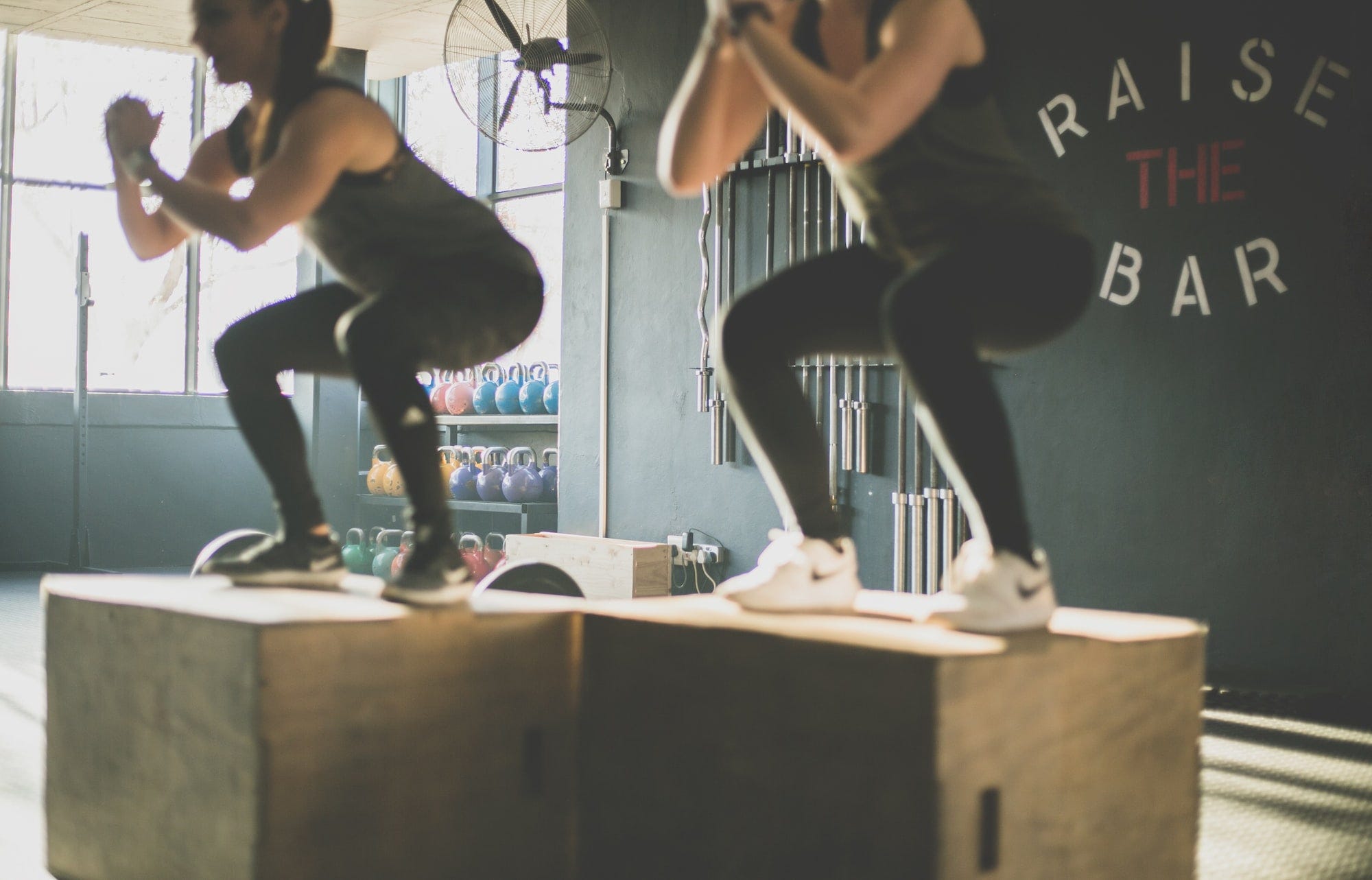 Two women squating on top of wooden blocks in a gym