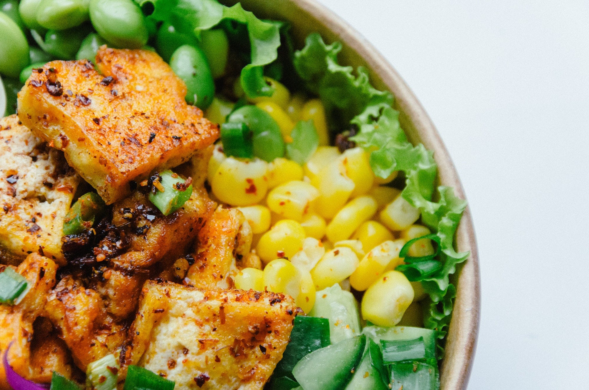 A bowl containing tofu, corn, and other green vegetables