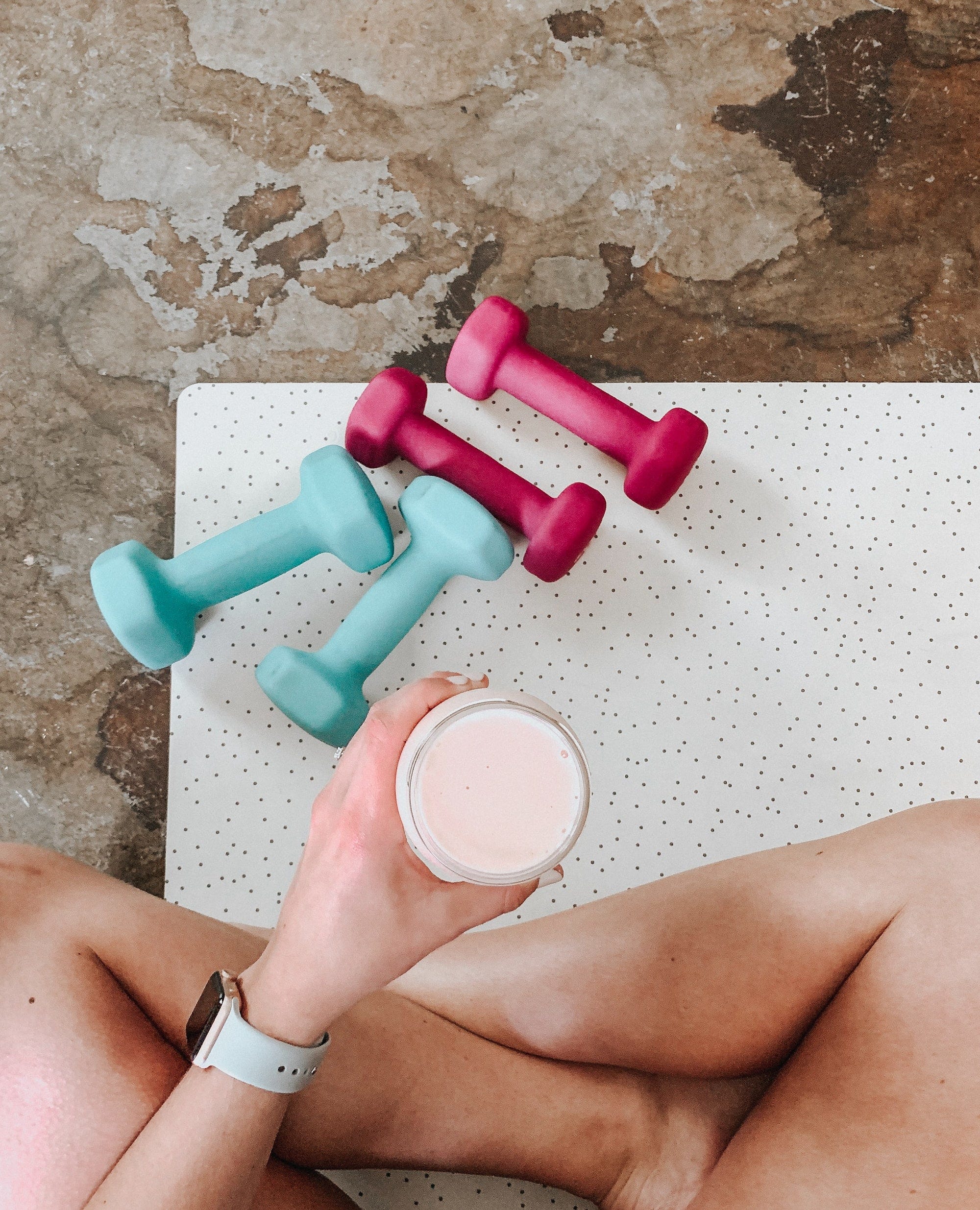 A woman taking a smoothie on her exercise mat which has weights on it