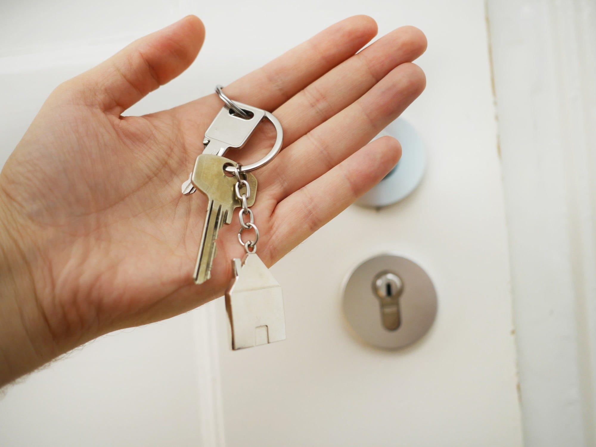 A set of keys on someone's palm with the door in the background