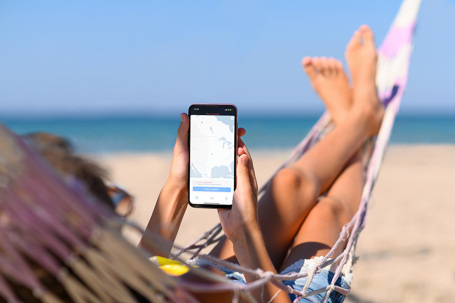 A woman connecting scroling the NordVPN app on her phone at a beach | Why You Need an eSIM for the Paris 2024 Olympics | Mania Tech